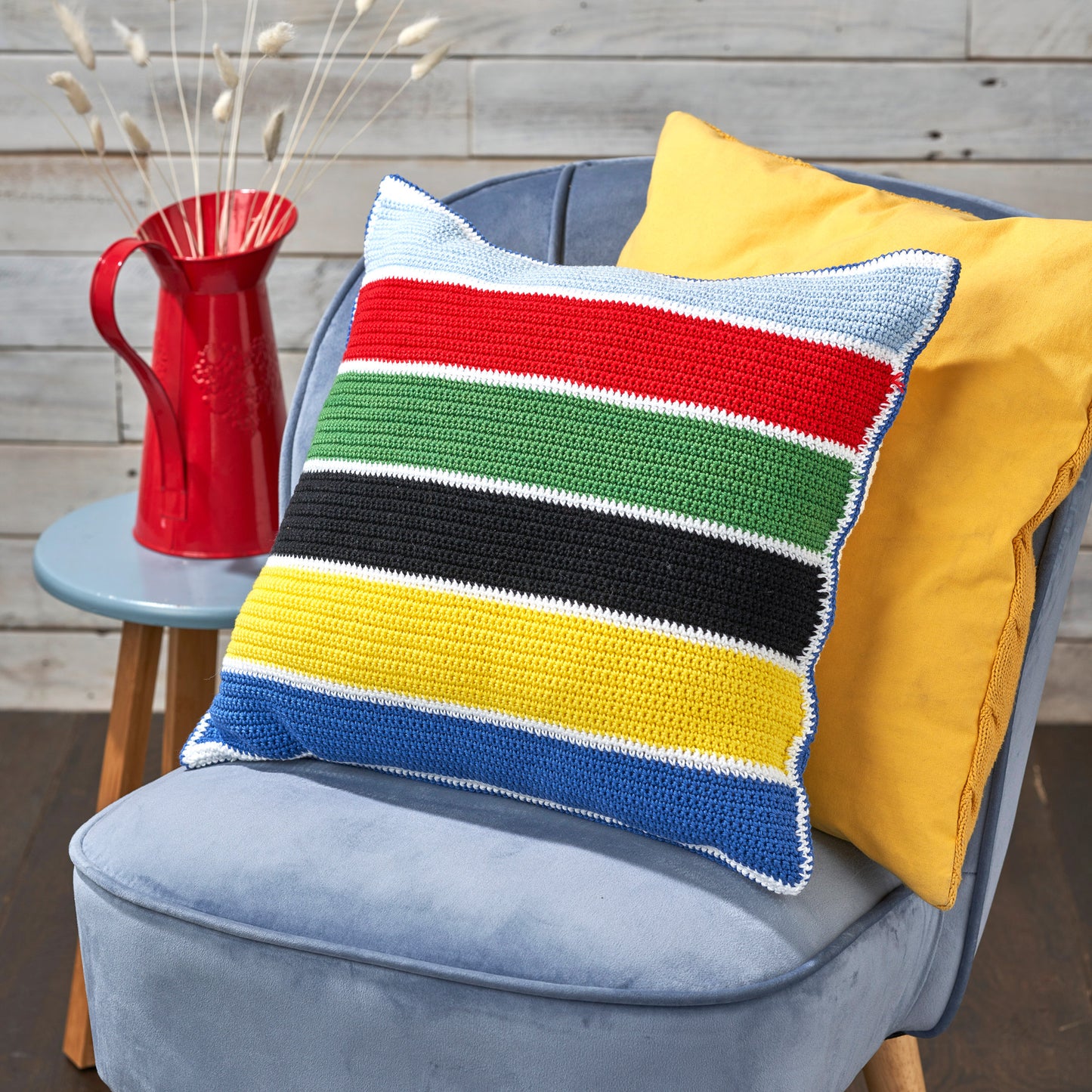 Colorful striped pillow on a chair with a red pitcher in the background