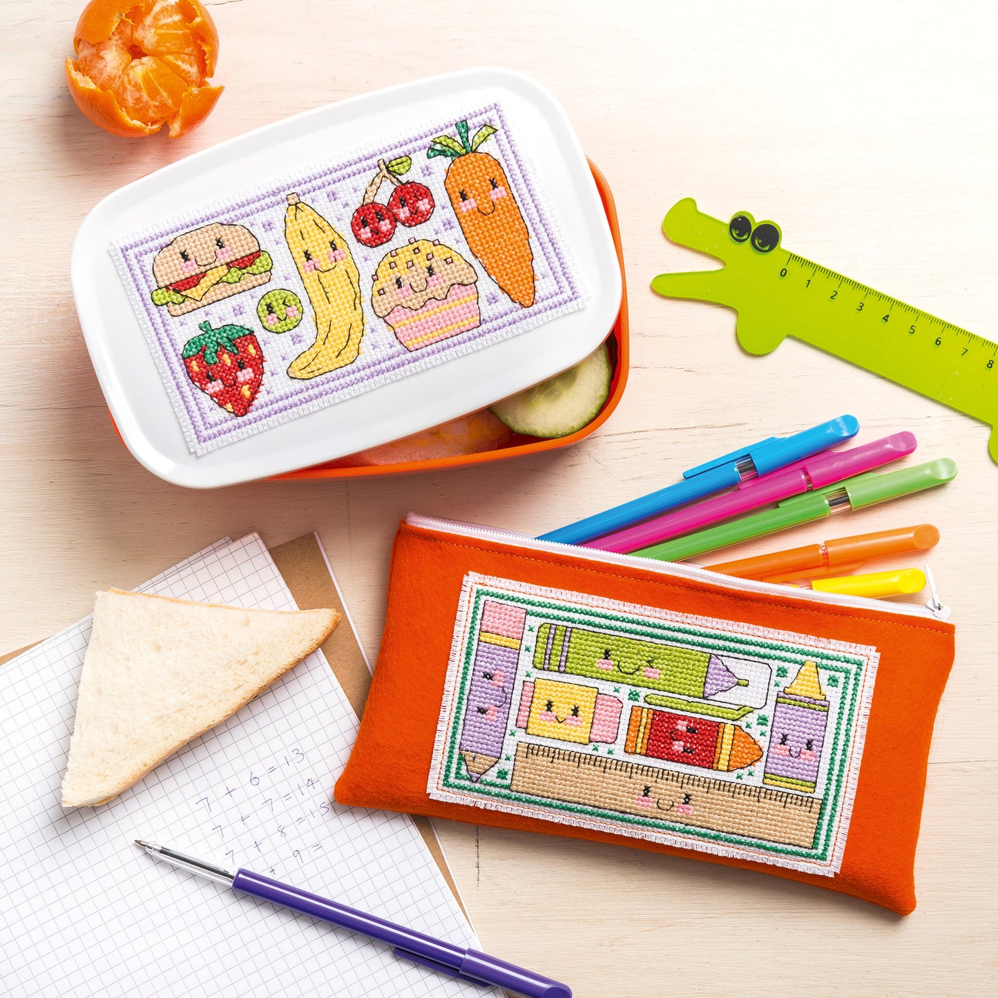 Cross-stitched pencil case and lunch box with food illustrations on a wooden surface.
