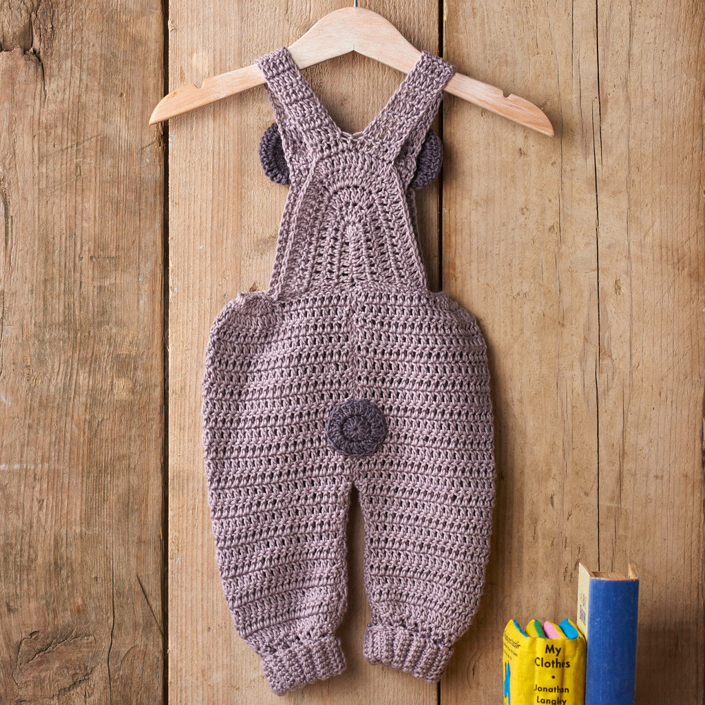 Crocheted baby overalls on a wooden hanger against a wooden background