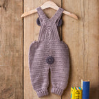 Crocheted baby overalls on a wooden hanger against a wooden background