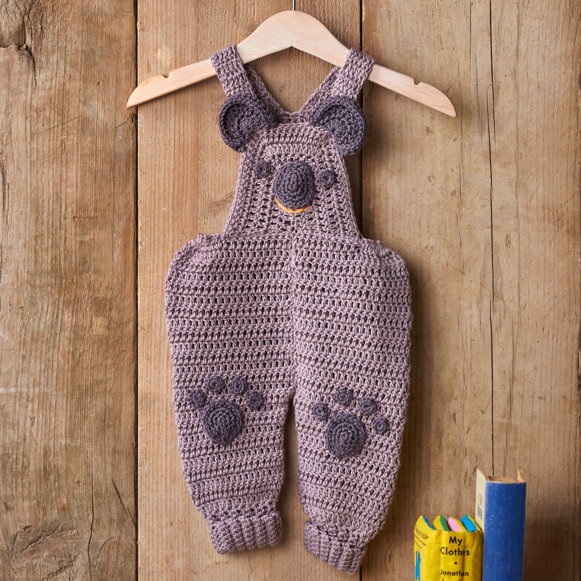 Crocheted baby overalls with paw prints on a wooden background