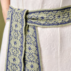 Green and blue patterned belt tied around a white garment