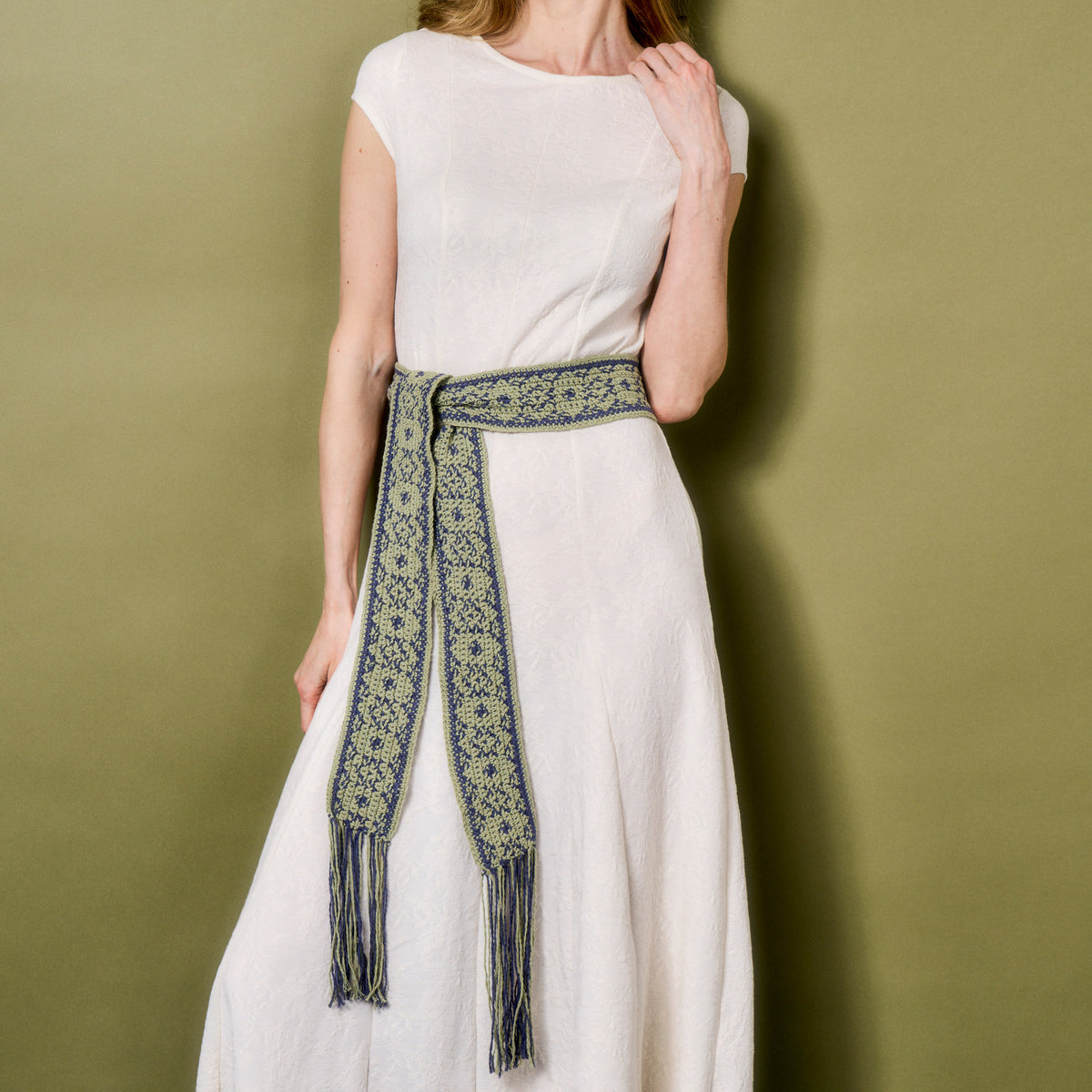 Woman wearing a white dress with a green patterned belt against a green background
