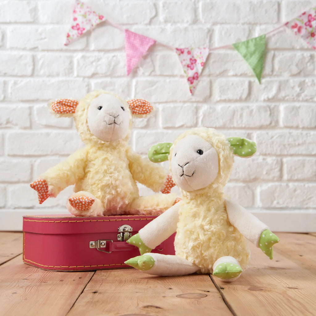 Two fluffy toy sheep with a red suitcase against a white brick wall with colorful bunting.