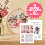 Embroidery hoop with floral bike design and PDF pattern on a wooden surface.