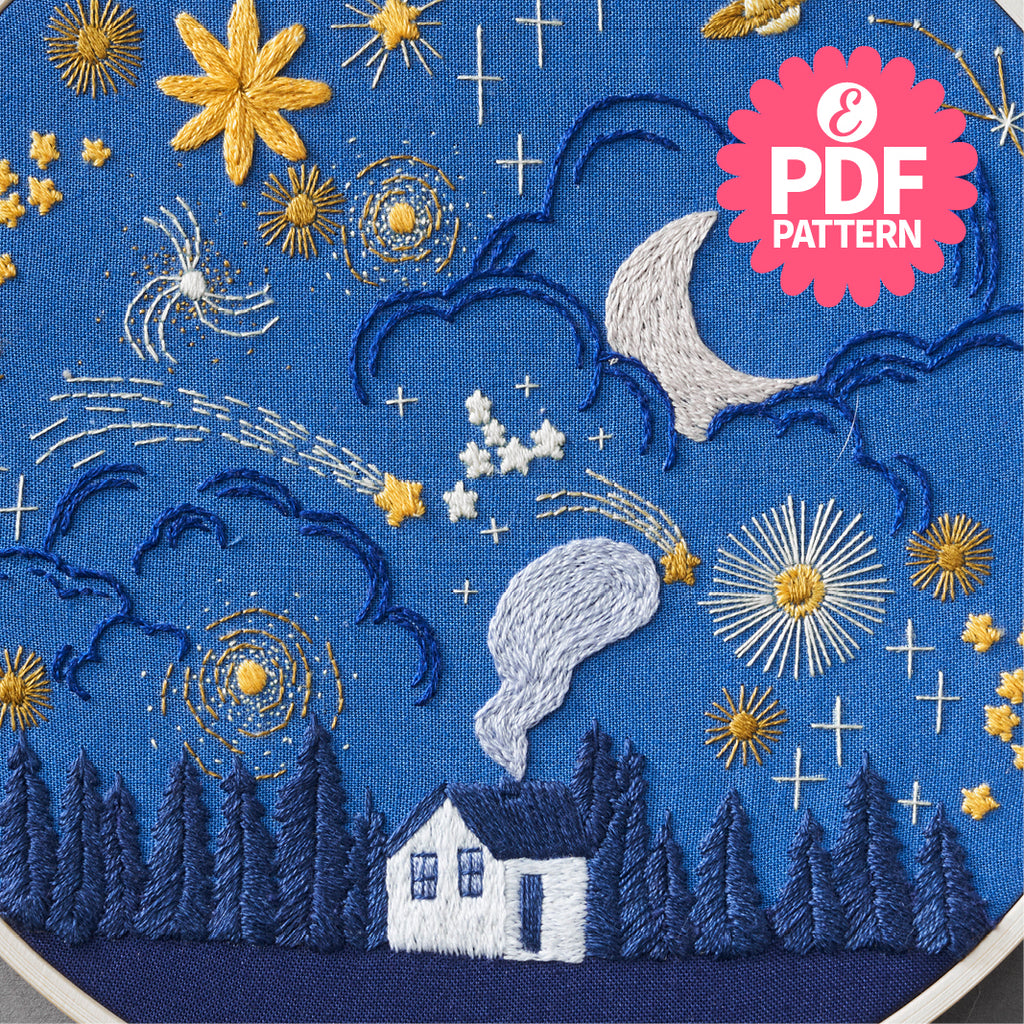 Embroidered design of a house, trees, and celestial elements on blue fabric with PDF pattern label.