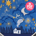 Embroidered design of a house, trees, and celestial elements on blue fabric with PDF pattern label.