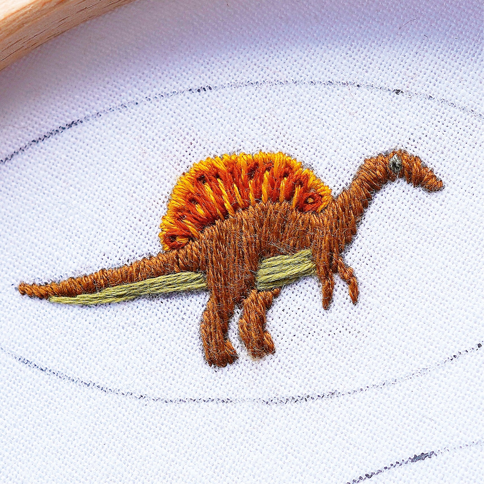 Embroidered dinosaur design on white fabric with a wooden hoop.