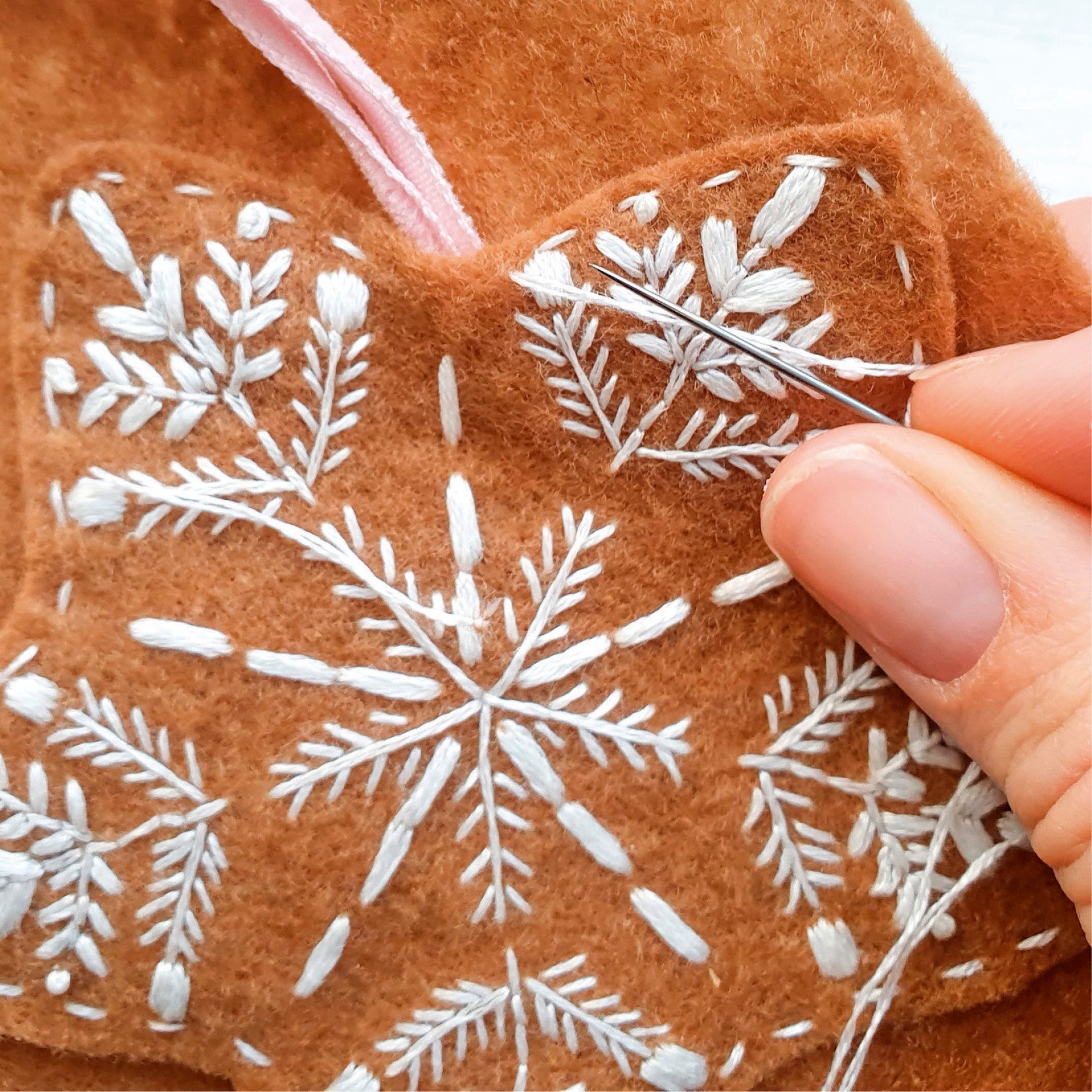 Close-up of hand embroidery on brown fabric with white snowflake patterns