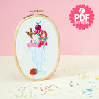 Embroidery hoop with a milkshake design on a pink background, featuring sprinkles and a cherry.