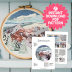 Embroidery hoop with mountain landscape design and embroidery guide on a wooden surface