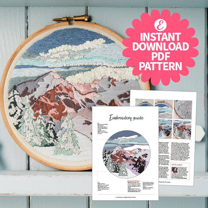 Embroidery hoop with mountain landscape design and embroidery guide on a wooden surface