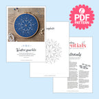 Embroidery hoop with blue design and related materials on a light blue background