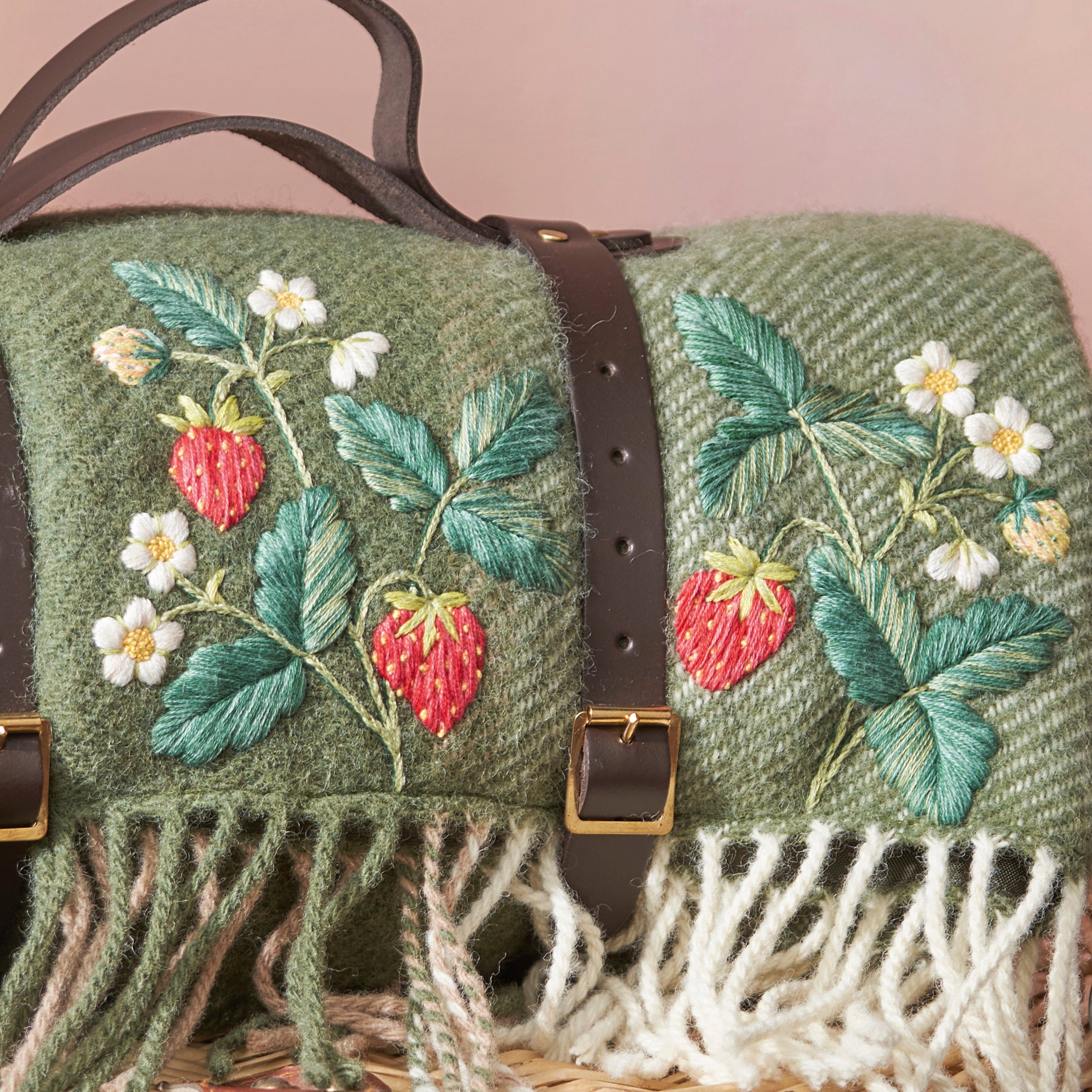 Green textured bag with embroidered strawberries and leaves on a pink background