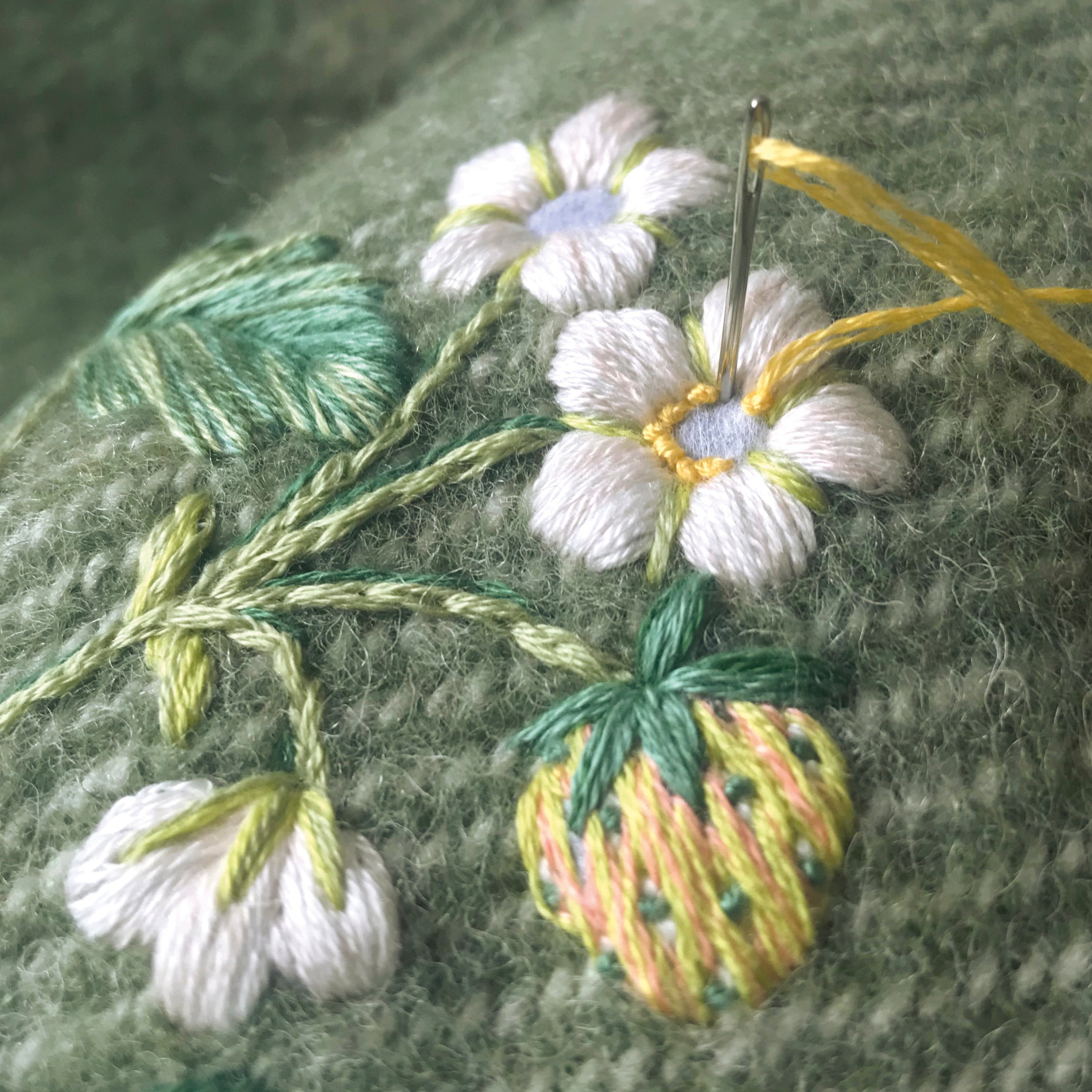 Embroidery of flowers and leaves on fabric with a needle and thread.