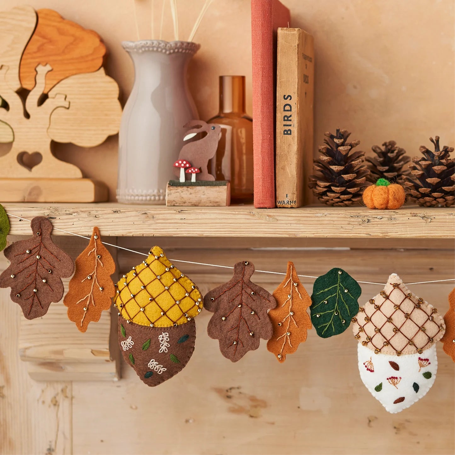 Decorative felt acorn and leaf garland on a wooden shelf with books and decorative items.