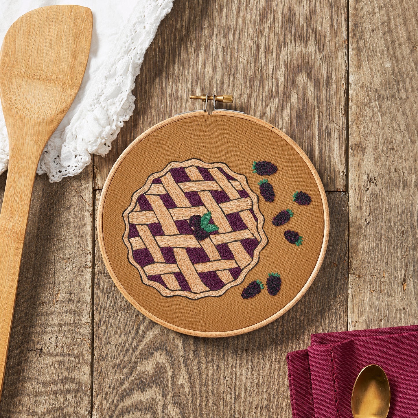 Embroidery hoop with a pie design on a wooden surface with kitchen items.
