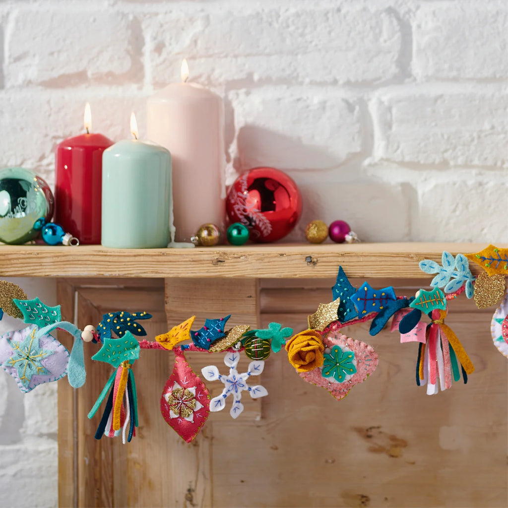 Decorative garland with colorful tassels on a wooden shelf with candles and ornaments.