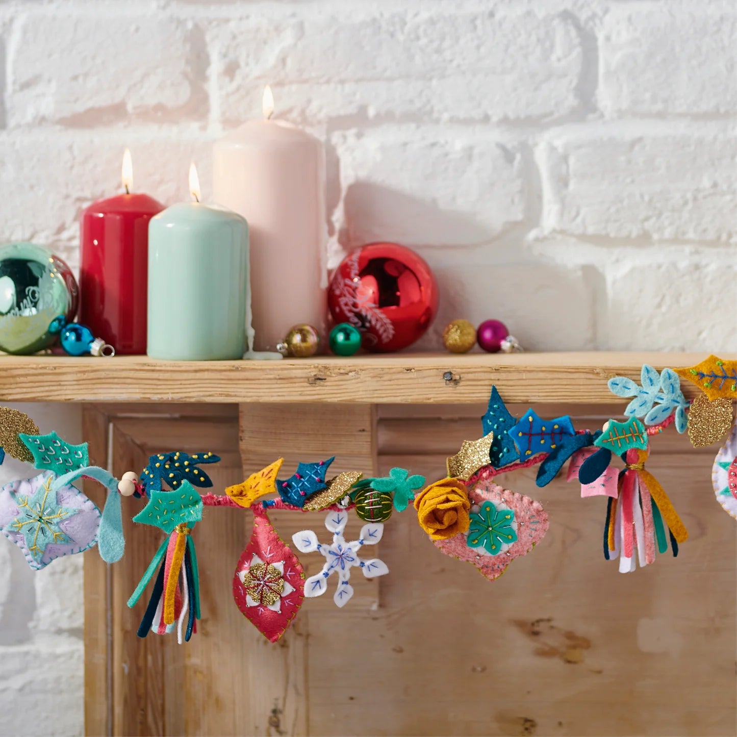 Decorative garland with colorful tassels on a wooden shelf with candles and ornaments.