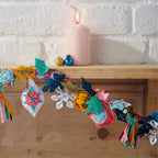 Decorative garland with colorful tassels and flowers on a wooden mantel with a lit pink candle.