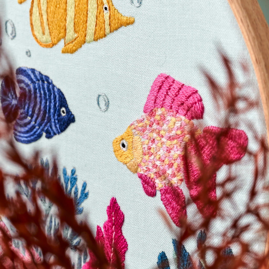 Embroidery hoop with colorful fish and coral design on a white background