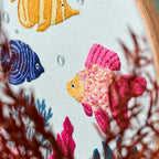 Embroidery hoop with colorful fish and coral design on a white background