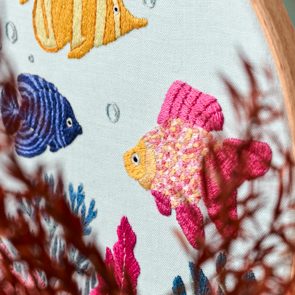 Embroidery hoop with colorful fish and coral design on a white background