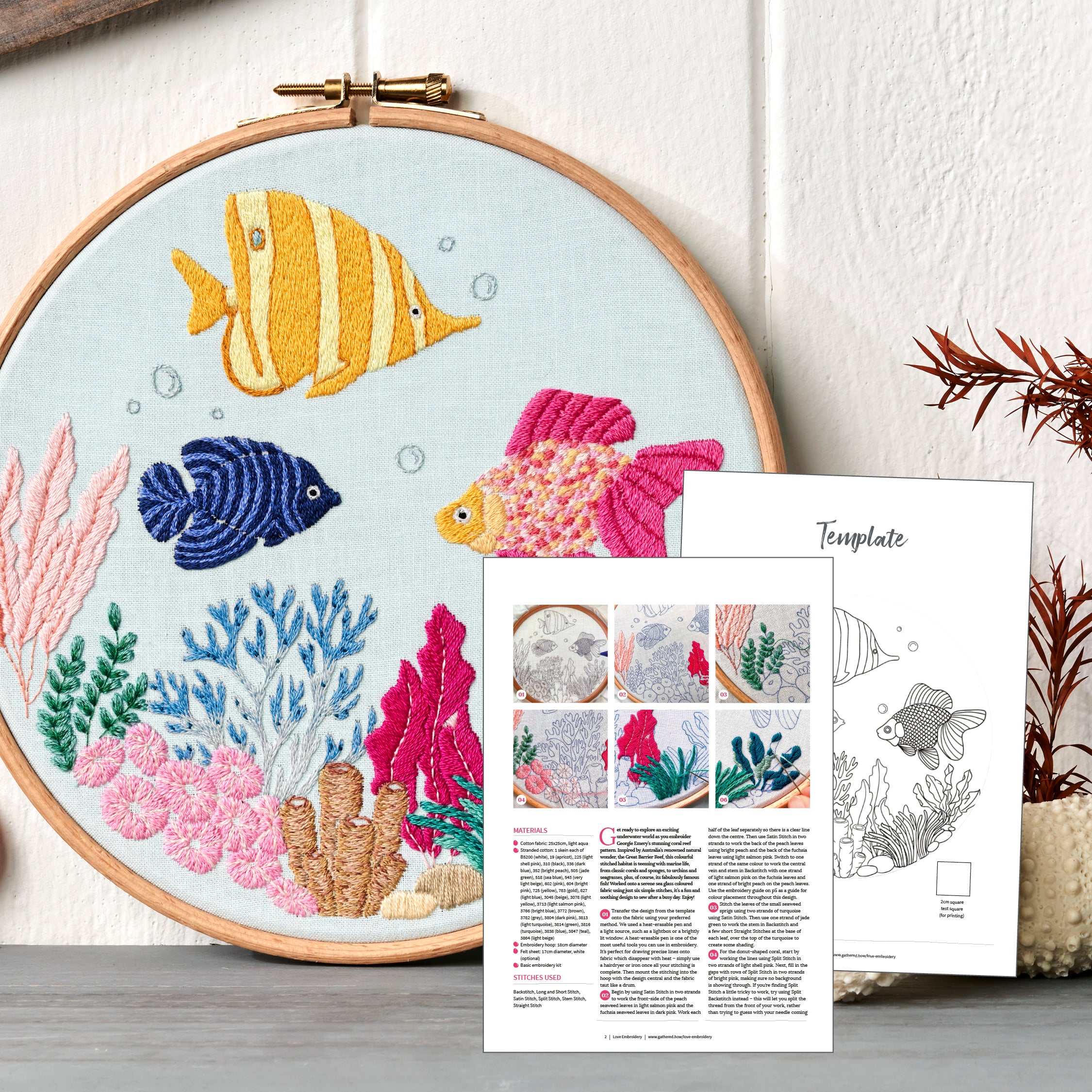Embroidery hoop with colorful fish design and an accompanying template sheet on a wooden surface.