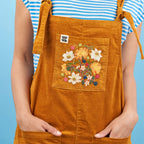 Person wearing a mustard yellow apron with floral embroidery on a blue background