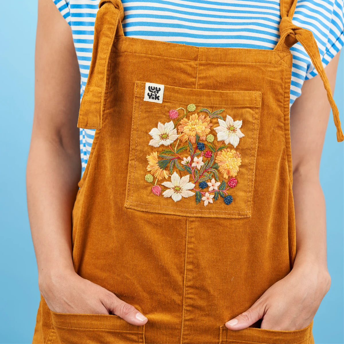 Person wearing a mustard yellow apron with floral embroidery on a blue background