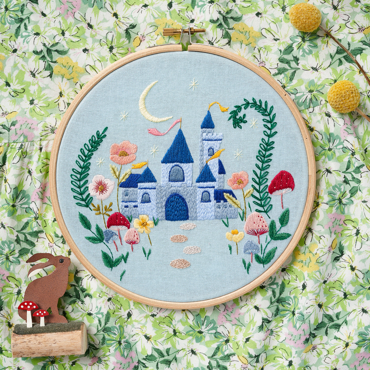 Embroidery hoop with a colorful castle design on a floral background
