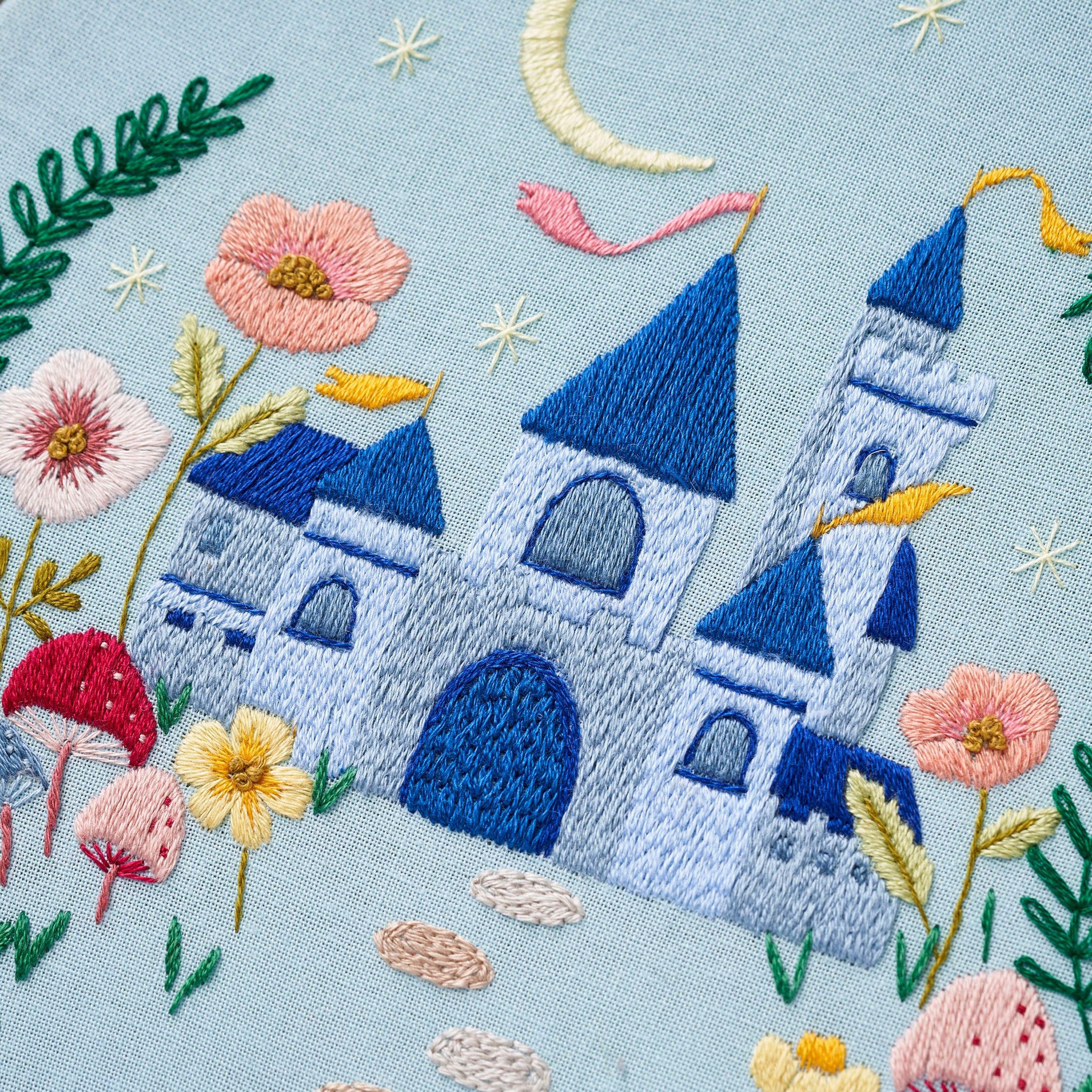 Embroidered design of a castle with flowers and plants on a light blue background