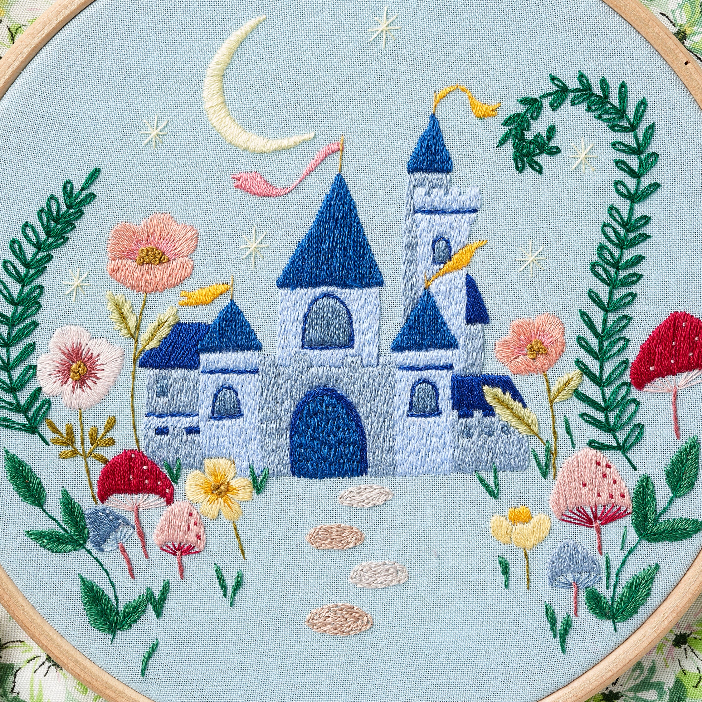 Embroidery hoop with a castle and floral design on a light blue background