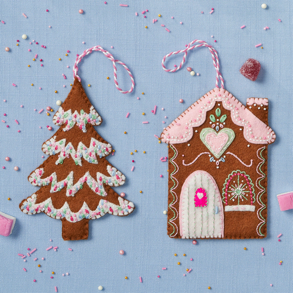 Felt gingerbread house and tree ornaments on a blue background with sprinkles.