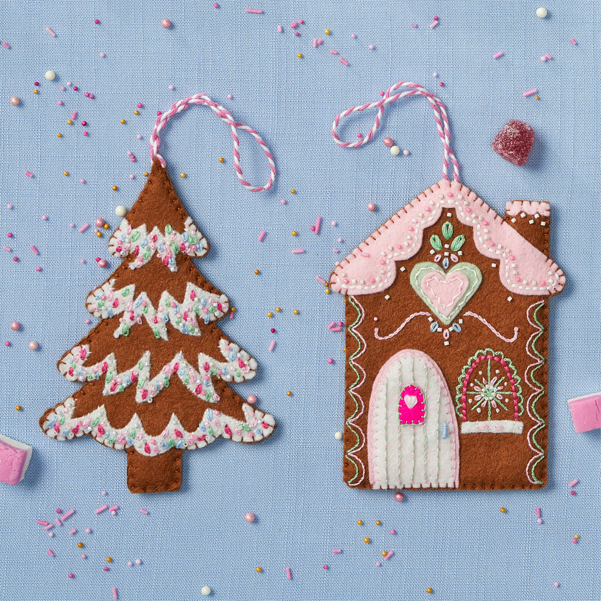 Felt gingerbread house and tree ornaments on a blue background with sprinkles.