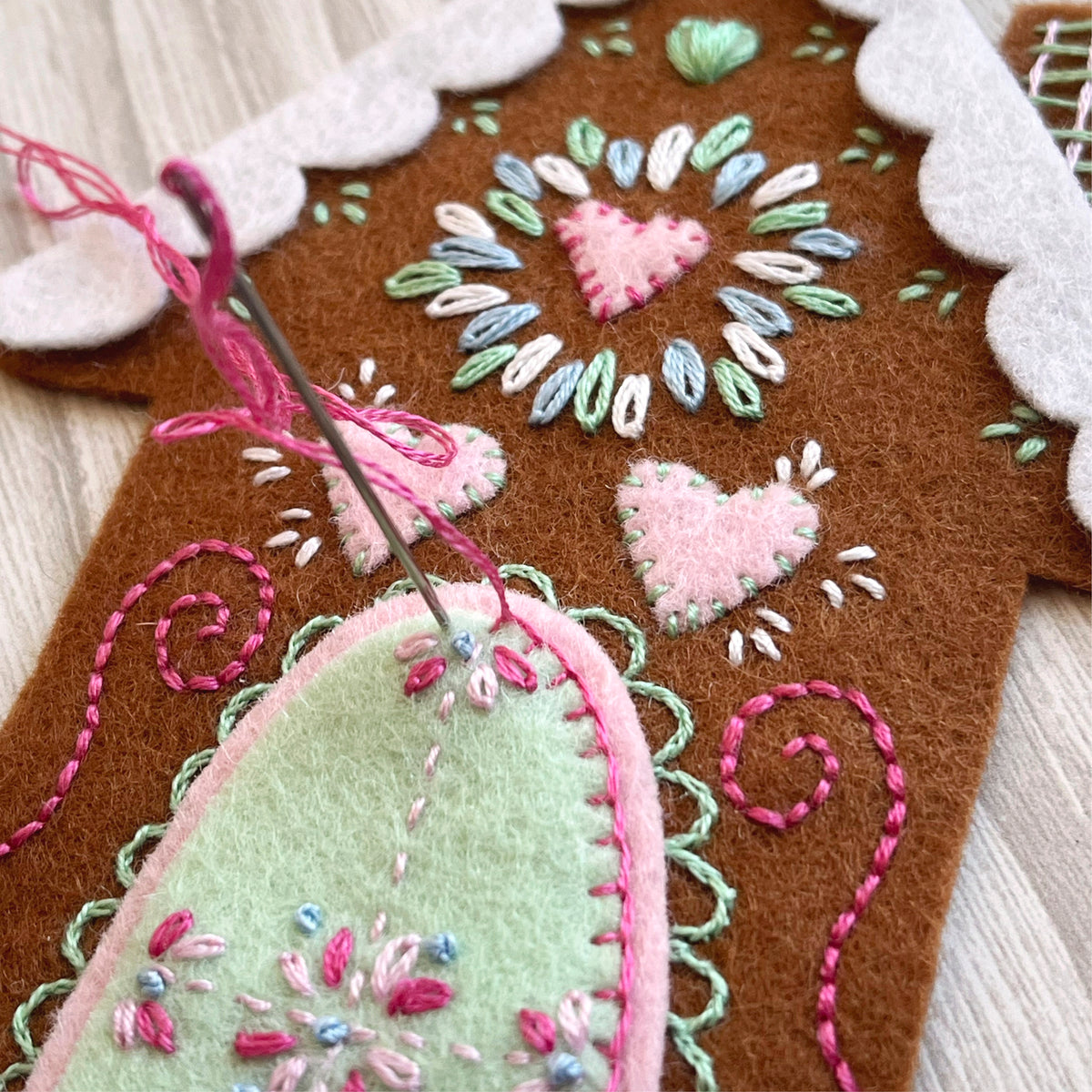 Embroidered felt heart shapes with pink, green, and white thread on a wooden surface.