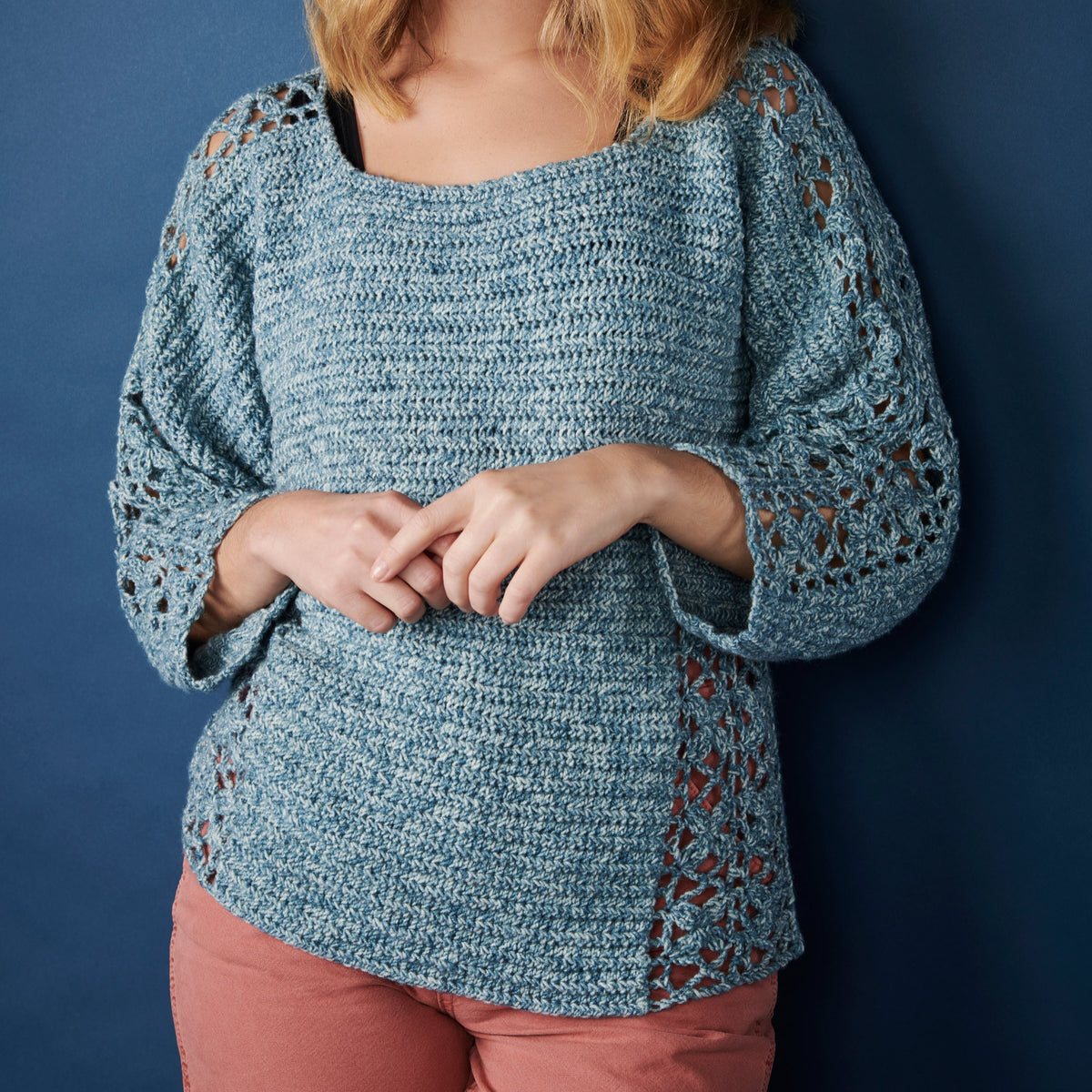 Person wearing a blue crochet sweater with floral patterns against a dark blue background