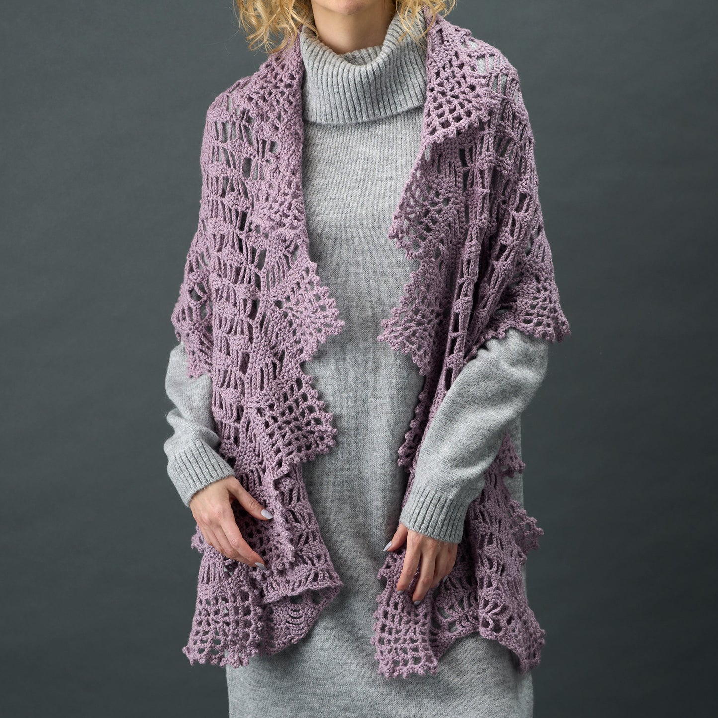 Person wearing a light purple lace cardigan over a gray dress against a dark background