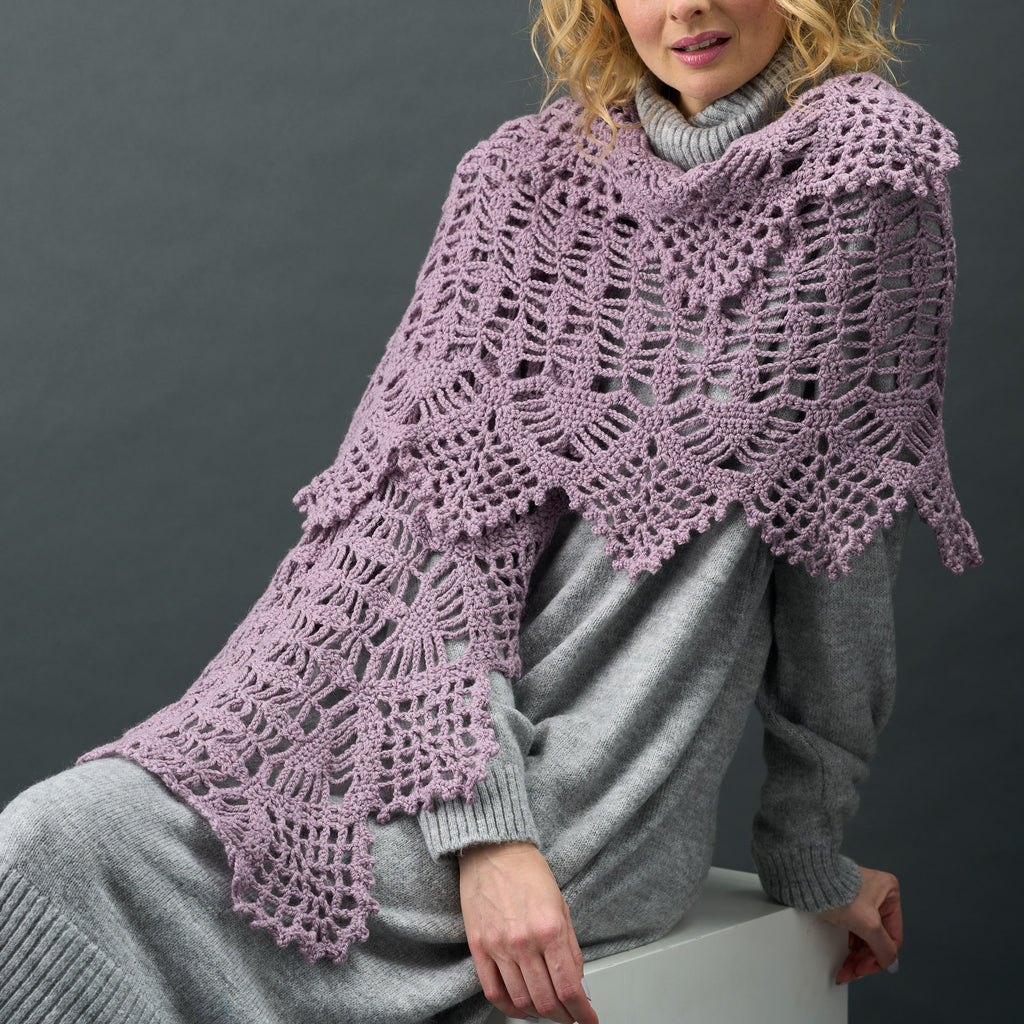 Person wearing a purple crocheted shawl over a gray outfit against a dark background
