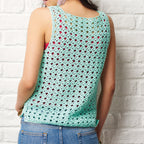Person wearing a green crochet tank top against a white brick wall.