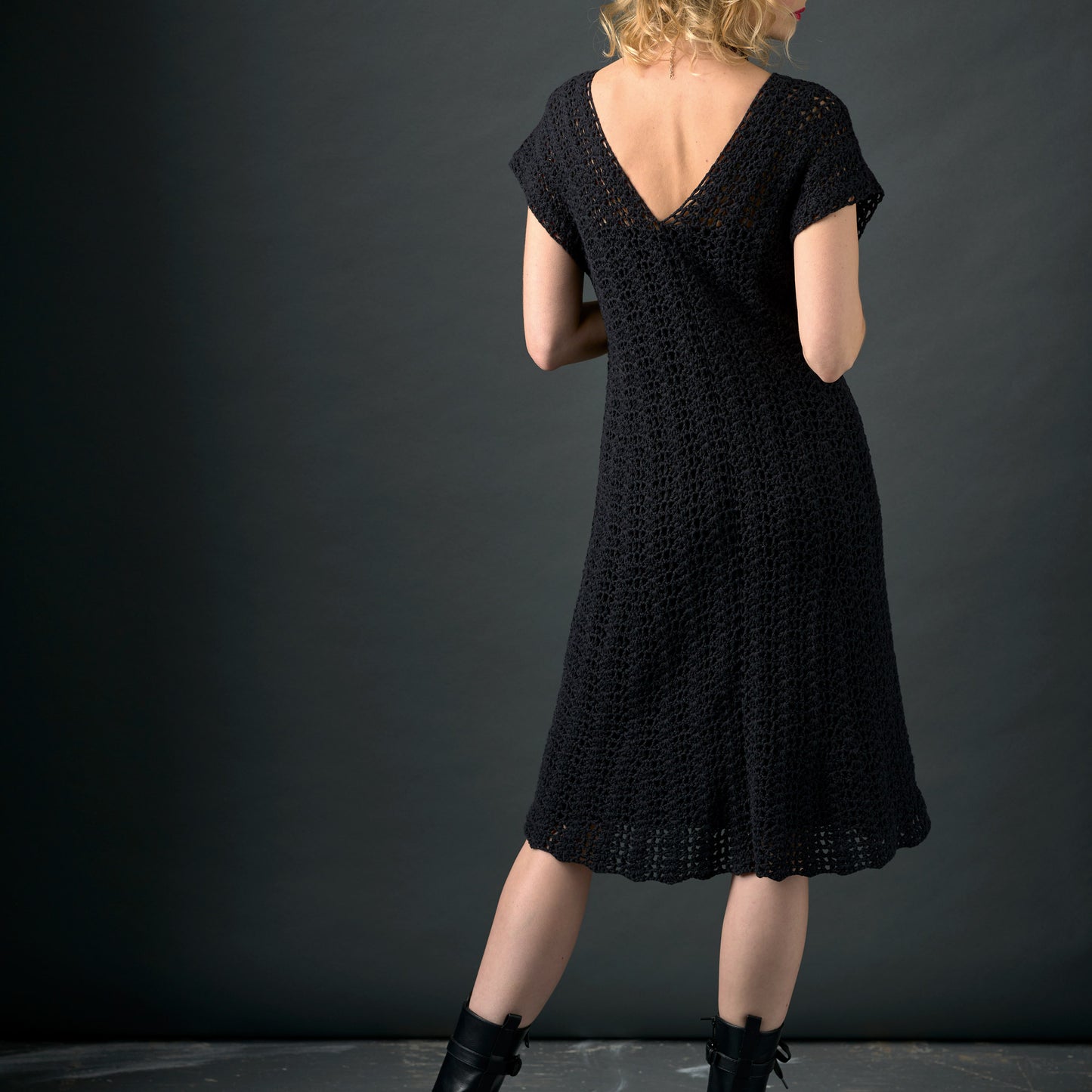 Person wearing a black dress with a textured pattern against a dark background