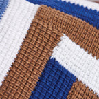 Close-up of a crocheted fabric with a striped pattern in white, brown, and blue. The textured stitching creates a cozy, handcrafted feel.
