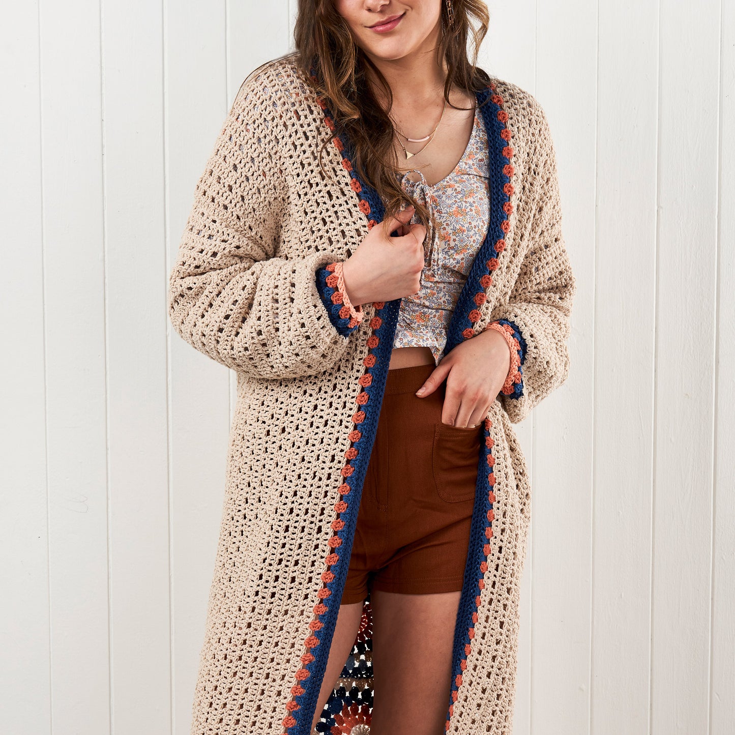 Woman wearing a long, patterned crochet cardigan against a white background
