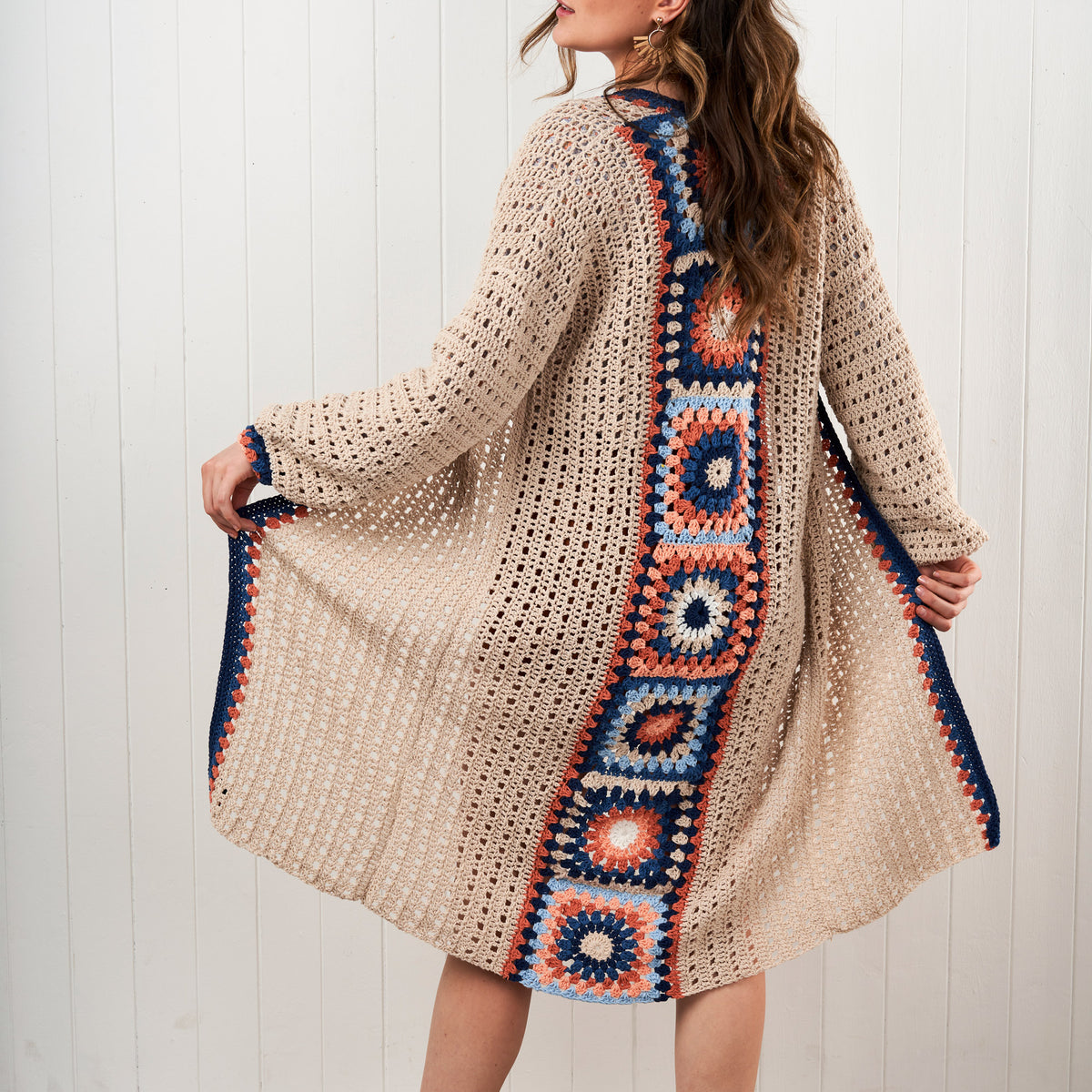 Woman wearing a beige crochet cardigan with colorful square patterns on a white background