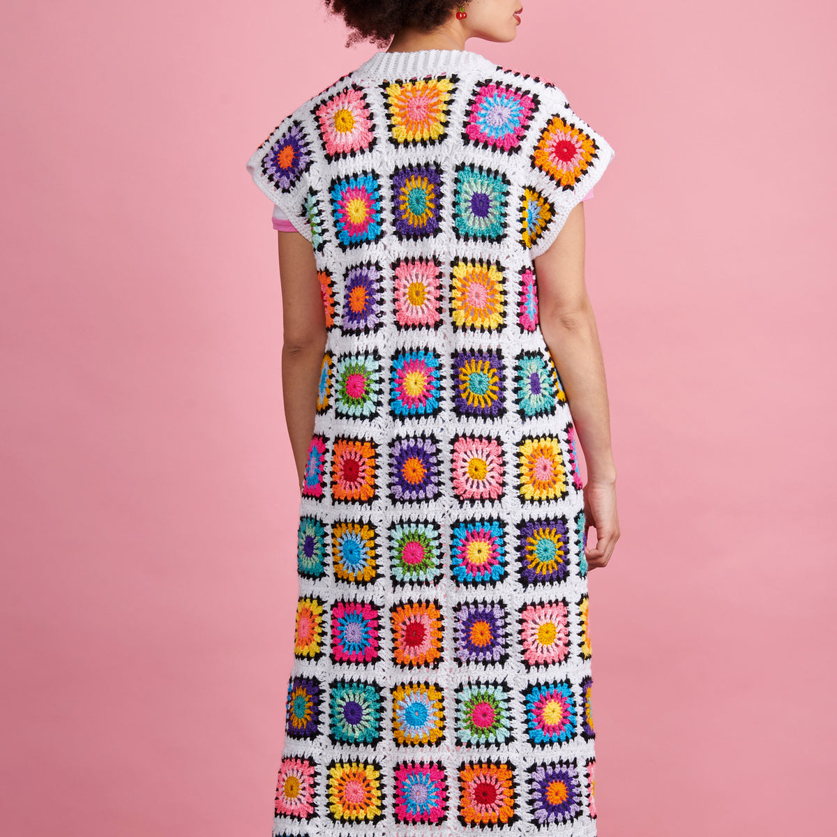 Person wearing a colorful crochet dress against a pink background