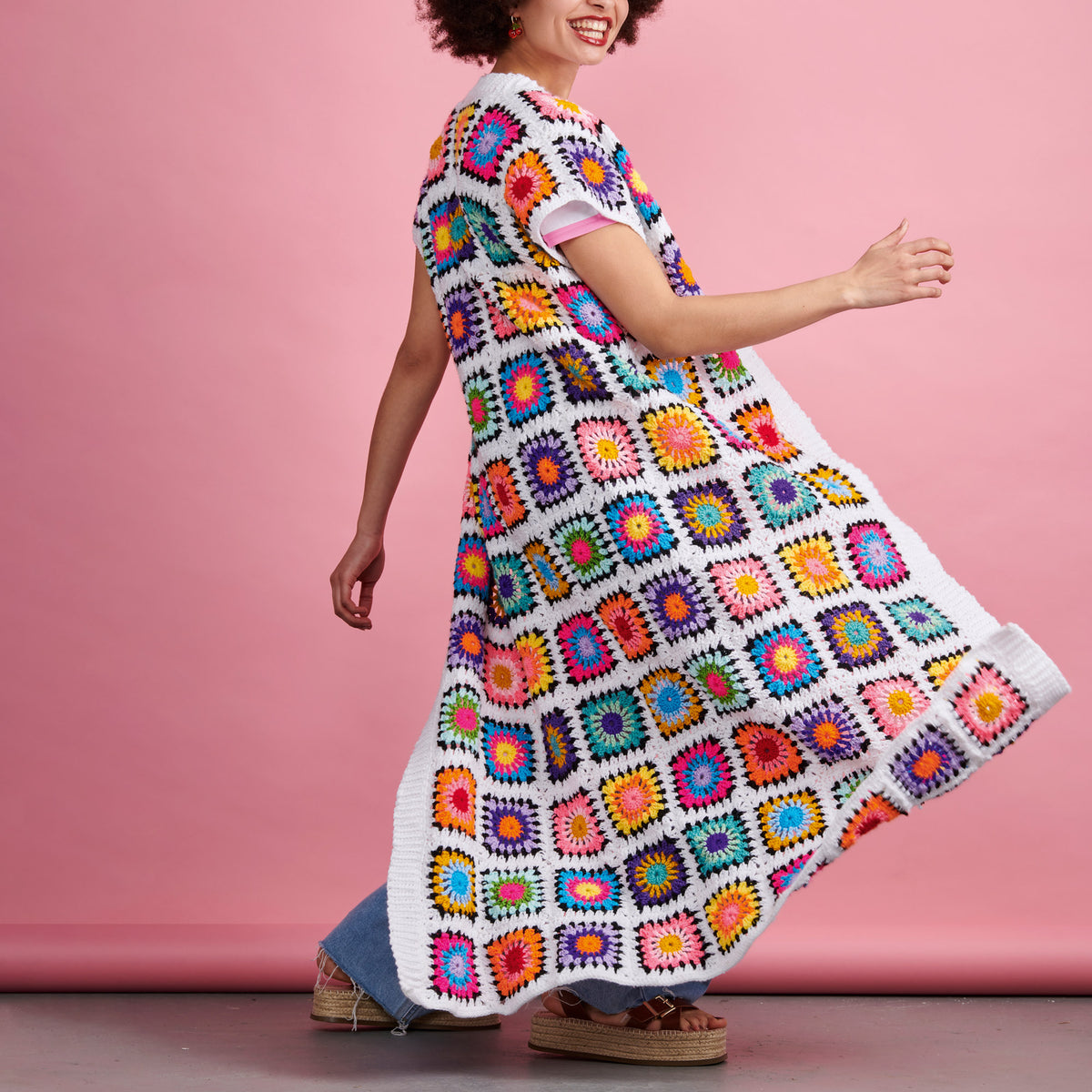 Woman wearing a colorful crochet dress against a pink background