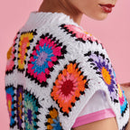 Person wearing a colorful crochet sweater with a pink background