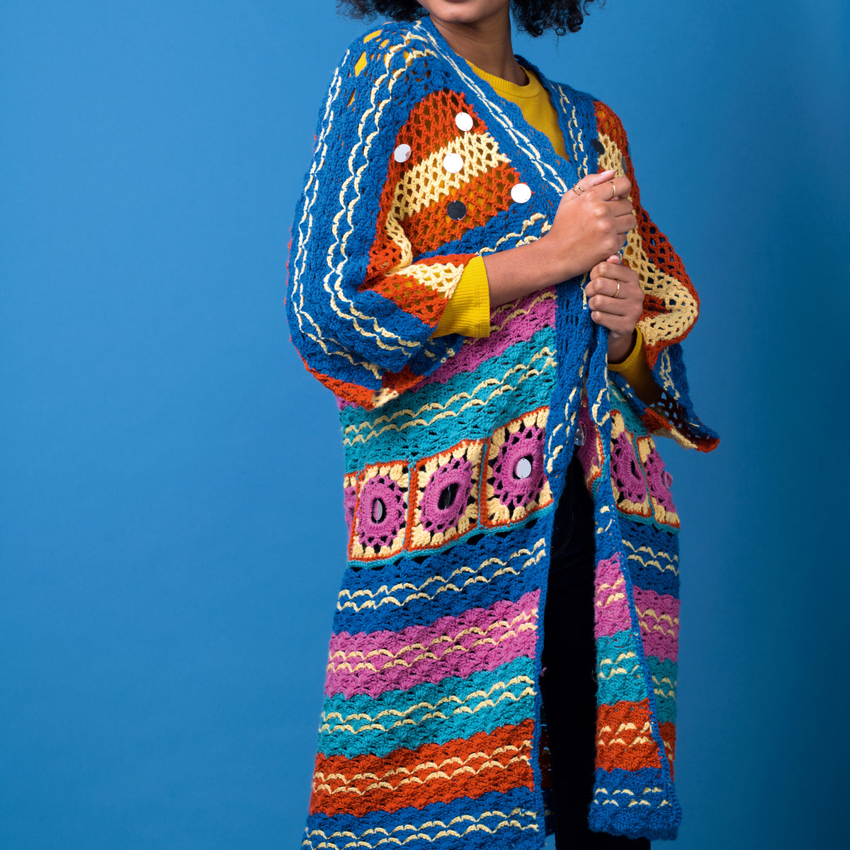 Person wearing a colorful crocheted cardigan against a blue background