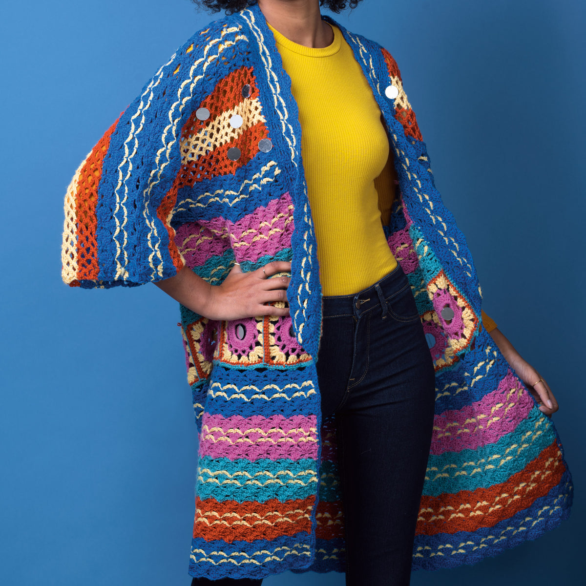 Person wearing a colorful crocheted cardigan against a blue background
