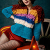 Person wearing a colorful knitted sweater sitting on a chair with a dark background